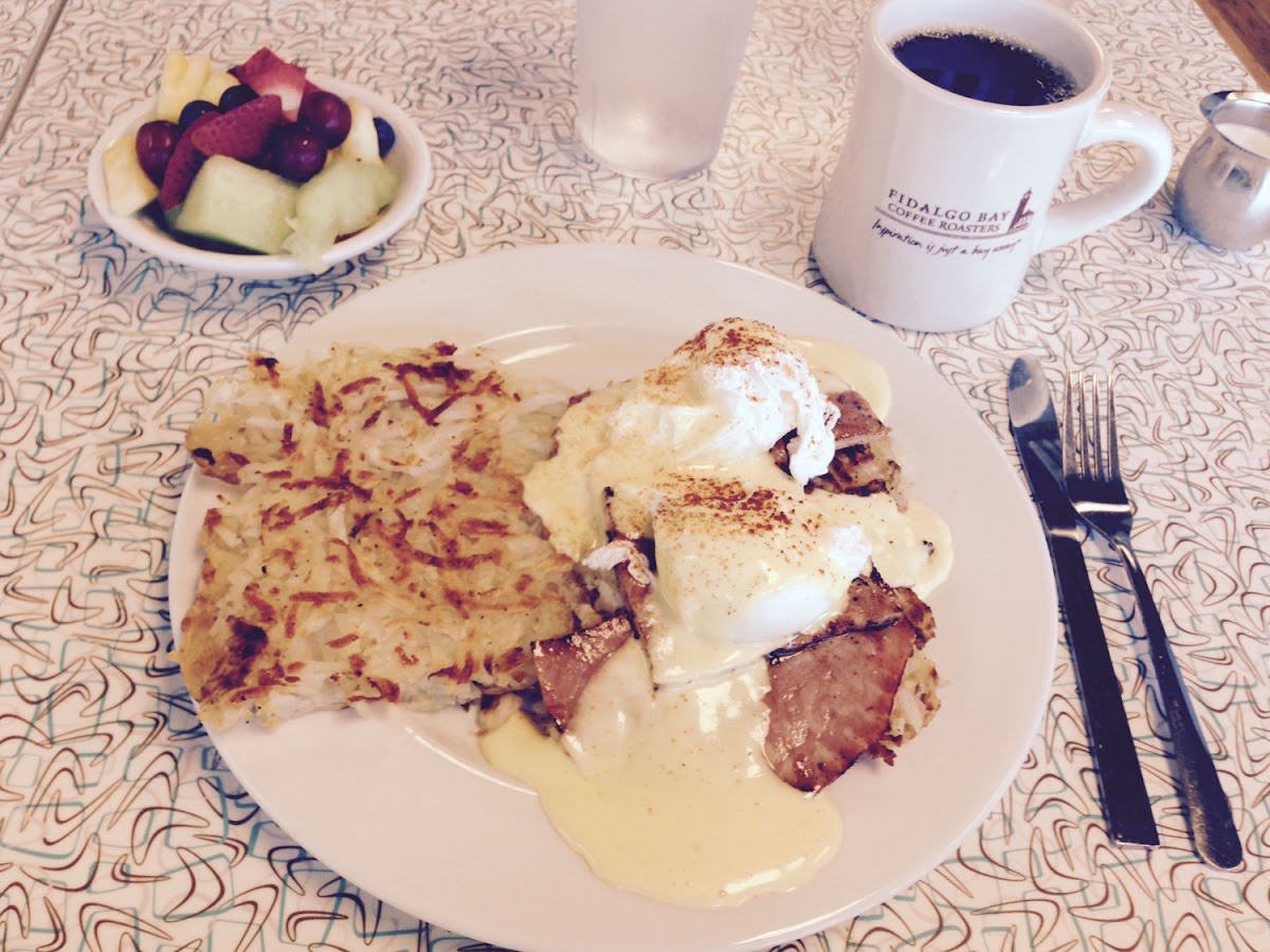 GF Eggs Benedict Over Ham With Hash Browns and a Side Of Fruit.