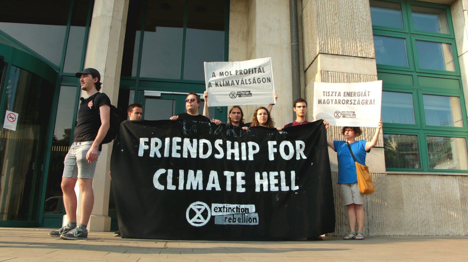 Rebels stand outside the ministry with a giant banner that says 'Friendship For Climate Hell'