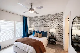 Model bedroom with an accent wall, upscale furniture, a ceiling fan, and large side by side picture windows