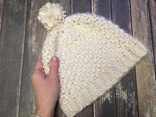 hand holding a crochet hat in front of wooden background