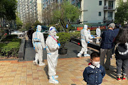 Medical workers in protective suits stand next to a line of residents waiting to take nucleic acid test at a locked down residential area, following the coronavirus disease (Covid-19) outbreak in Shanghai, China April 7, 2022.