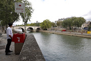 A journalist poses as he stands in front of a bright red, eco-friendly urinal on the Ile Saint-Louis along the Seine River in Paris, France, August 13, 2018. 