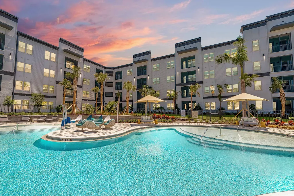 Resort-style swimming pool with lounge chairs and apartment buildings in the background at dusk