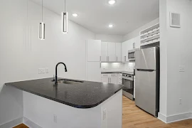 Modern apartment kitchen with white cabinets, stainless steel appliances, and a central island with a sink.