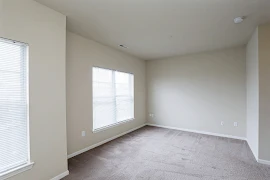 Corner of bedroom with neutral walls, white trim, neutral carpet, and three windows