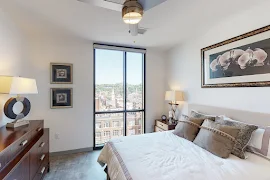 Bedroom with light walls, bed with light bedding, ceiling fan, and large windows