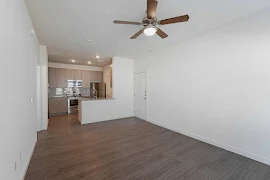 Living room with light walls and trim, wood-inspired flooring, ceiling fan, access to kitchen area, and view of entryway door