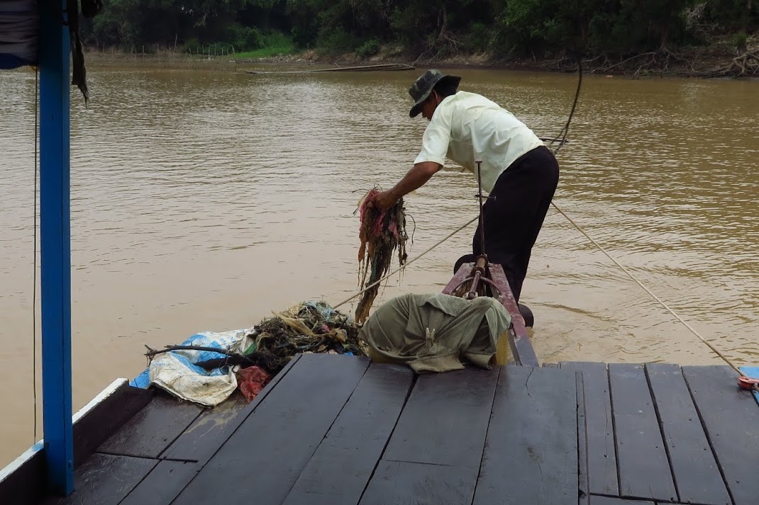 Our boatman removing debris from the propeller of our boat in the middle of our journey to Tonle Sap. This occurs several times during our boat ride.  