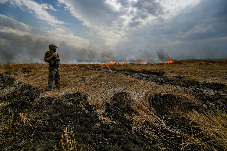 A Ukrainian serviceman stands on a burning wheat field on a border between Zaporizhzhia and Donetsk regions, Ukraine, July 17 2022. Picture: REUTERS/DMYTRO MOLIENKO