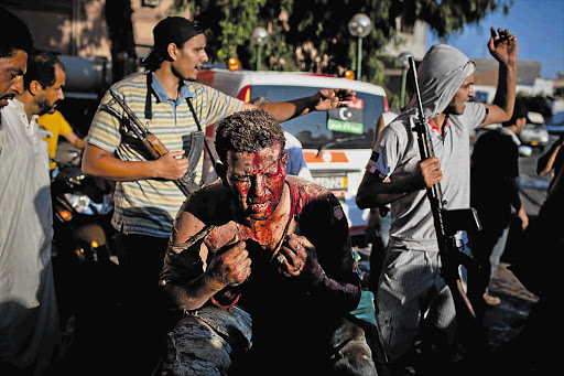 Libyan rebel fighters protect a pro-Gaddafi loyalist fighter from angry onlookers as he is brought in for medical attention to the Tripoli Central Hospital yesterday