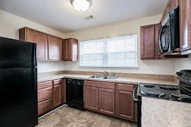 Kitchen with black appliances, wood cabinets, window with blinds over sink, tile patterned flooring, and dome light fixture