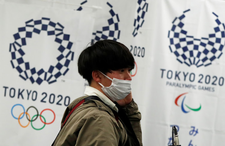 man wearing a protective face mask, following an outbreak of the coronavirus disease (COVID-19), walks in front of flags of the Tokyo 2020 Olympic and Paralympic Games in Tokyo