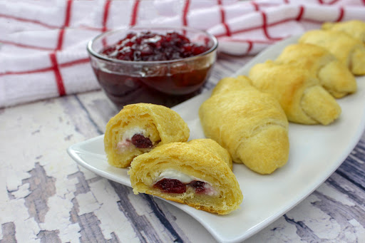 A tray of cranberry cream cheese crescent rolls with one cut open.