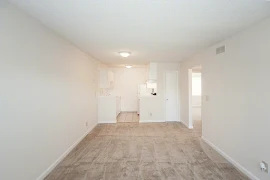 Living Area with neutral carpeting and walls looking onto kitchen with white cabinets and appliances