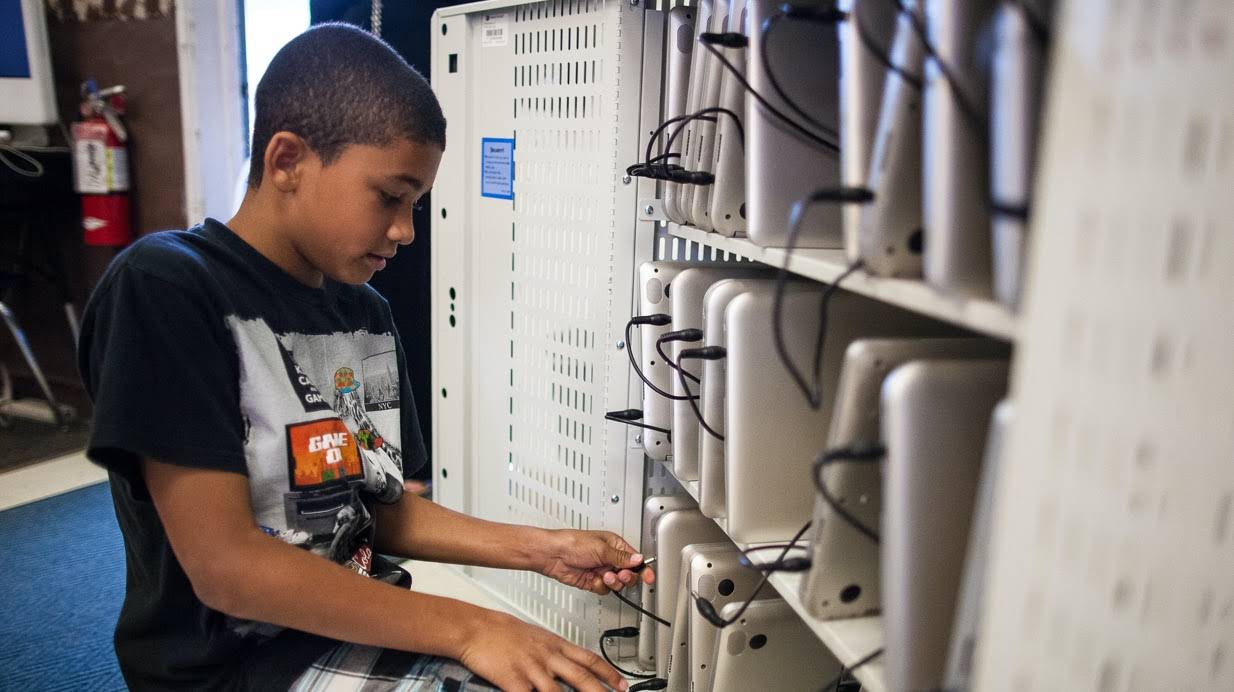 A student organizing Chromebooks on classroom shelves.