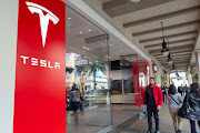 People walk past the brand's logo at a Tesla Motors store on Santana Row in the Silicon Valley, San Jose, California.
