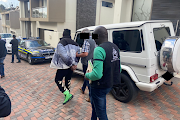 James Aliyu walks past his luxury Mercedes-Benz G63 SUV as he is taken into custody by Interpol officers.