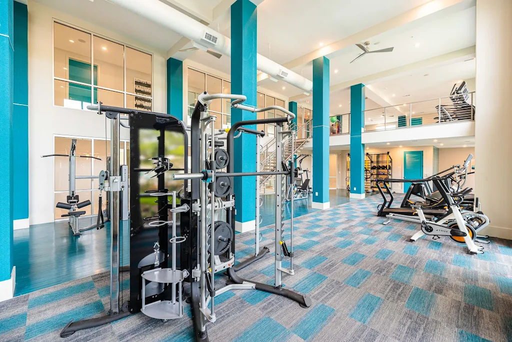 Two-story fitness center with weight and cardio machines. Large floor to ceiling windows and large ceiling fans.