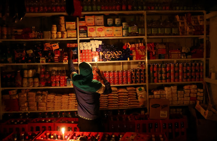 A shop owner picks an item for a customer by candlelight during power outages on April 20 2022. Picture: REUTERS/SiPHIWE SIBEKO