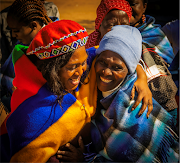The joy of the occasion is reflected in the faces of Lily Buhle Skosana (left in the Middelburg blanket) embracing Selina Skosana (in the blue blanket), who went home after a long night and day of cooking, to change and return for the celebrations with her family and friends.