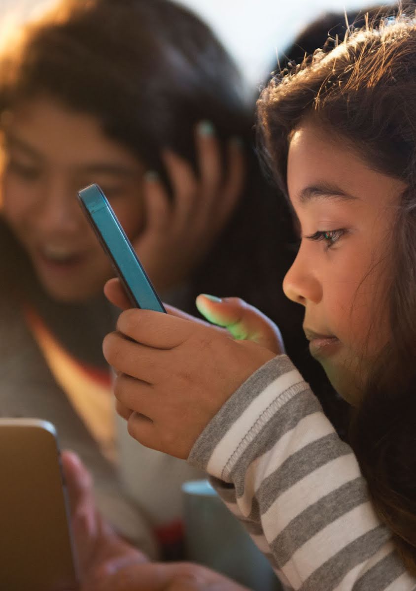 Una niña mira con atención su teléfono con un grupo de amigos.