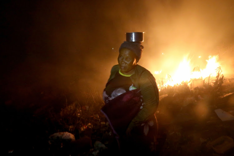 Nonsindiso Msizeni, 42, carries a stainless steel bowl she recovered with other items after her home was burnt to ashes.