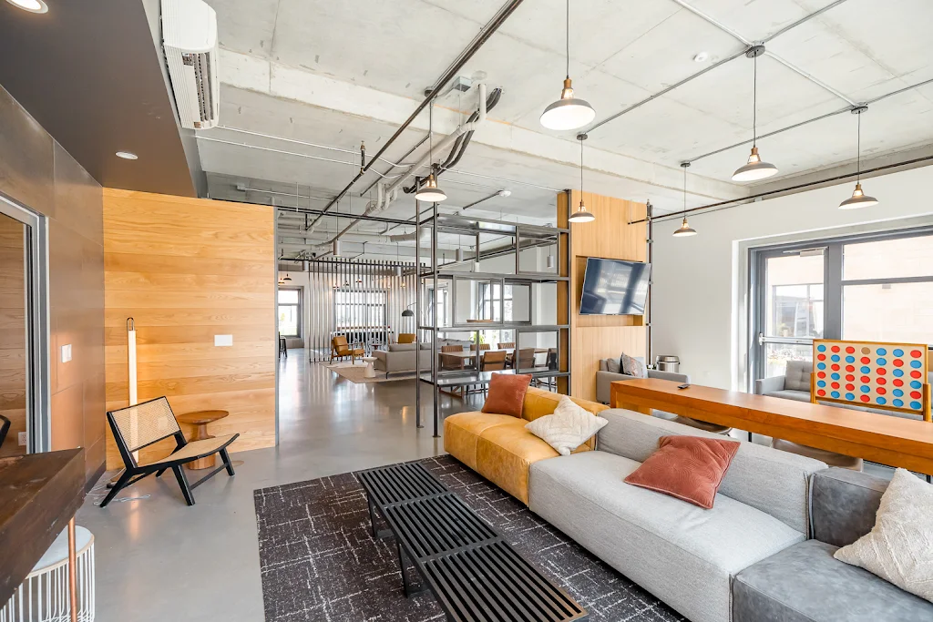 Lounge area in clubhouse with games, mounted TVs, several seating areas with couches and chairs, and hanging lights