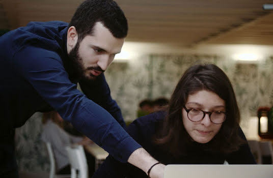 Un homme debout montre quelque chose sur l'écran à une femme assise devant un ordinateur.