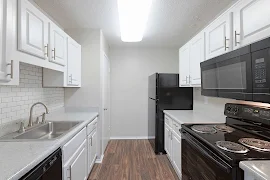 Modern apartment kitchen with white cabinets, subway tile backsplash, and black appliances.