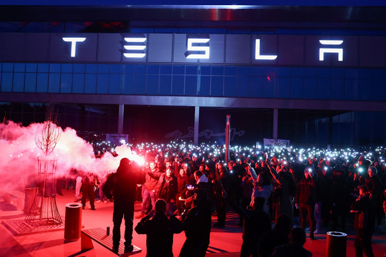 Workers of Tesla's plant near Berlin light up their phones as a man holds a lit flare in front of the so-called Gigafactory. Picture: CHRISTIAN MANG