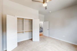 Bedroom with plush carpet, ceiling fan, neutral colored walls, and double door closet