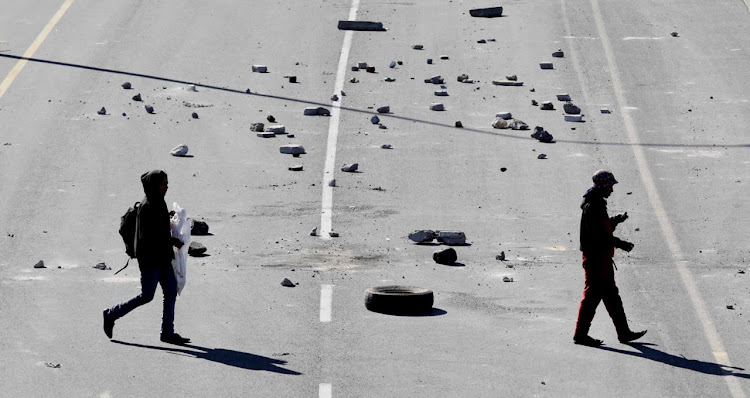 Residents near Samora Machel walk across the R300 which was barricaded on Wednesday by groups of people attempting to loot food delivery trucks.