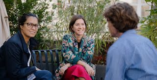Dos mujeres y un hombre mantienen una conversación amistosa con sonrisas en sus caras.