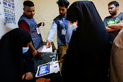 An Iraqi woman gets her fingerprints scanned to verify her identity before voting at a polling station during the parliamentary elections, in Sadr City, Baghdad, Iraq October 10, 2021. 