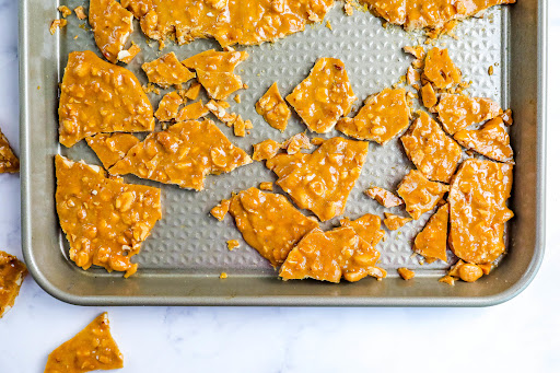 Broken pieces of Old-Fashioned Peanut Brittle on a baking pan.