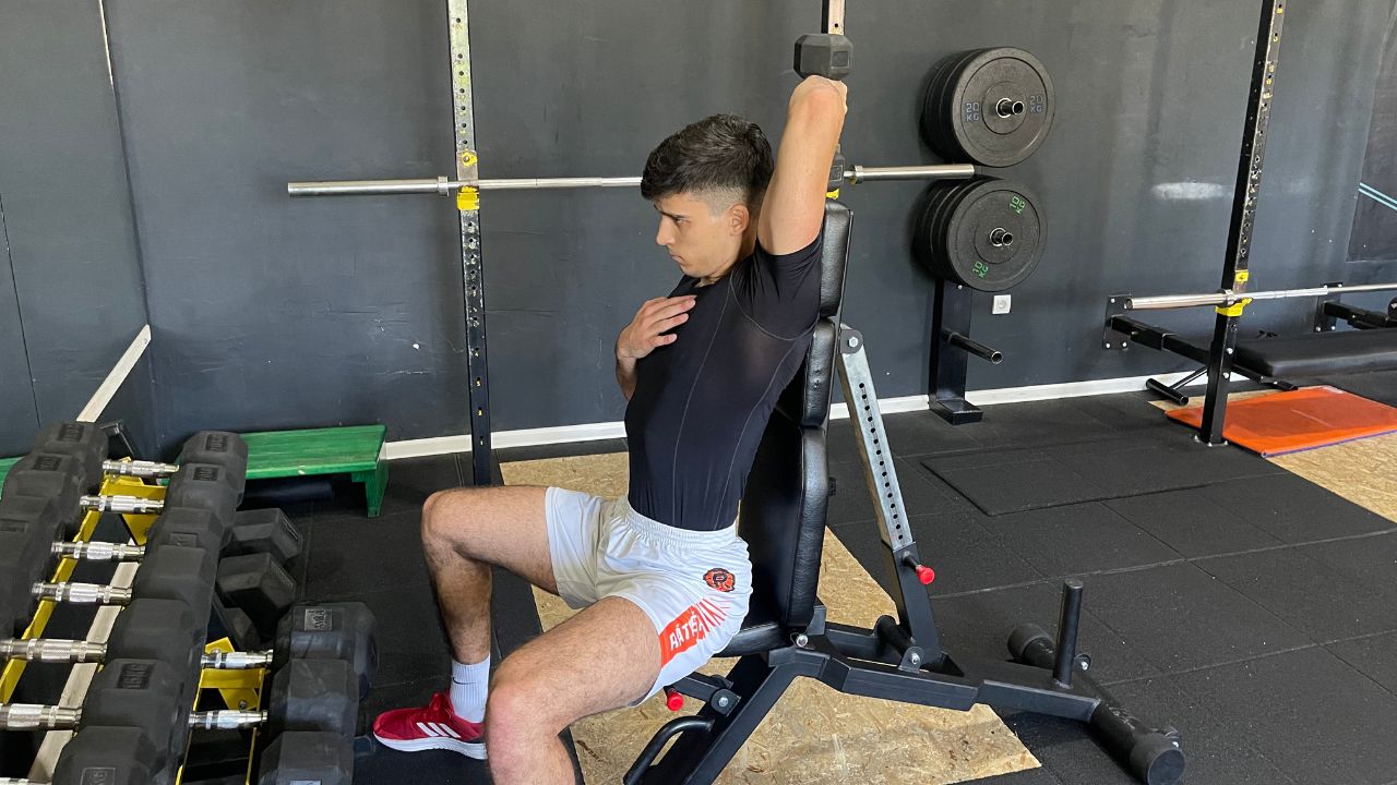 Vanja performs dumbbell overhead triceps extension.