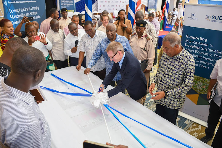 British High Commissioner Neil Wigan cuts the ribbon during the launch of the construction of the Lamu cashew factory. Looking on is Equatorial Nut Processors chairman Peter Munga and Lamu Governor Issa Timamy.