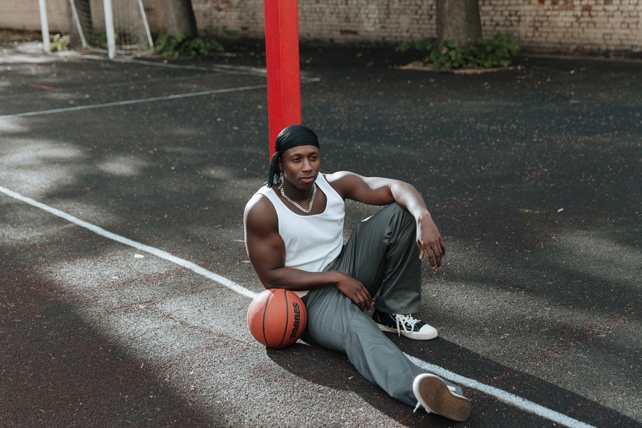 Mann sitzt mit einem Basketball und trägt Trainingshosen