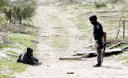 An injured protester is watched over by a Cape Town law enforcement officer after land invaders clashed with secuerity forces in Bloekombos, Cape Town, on August 8 2020.