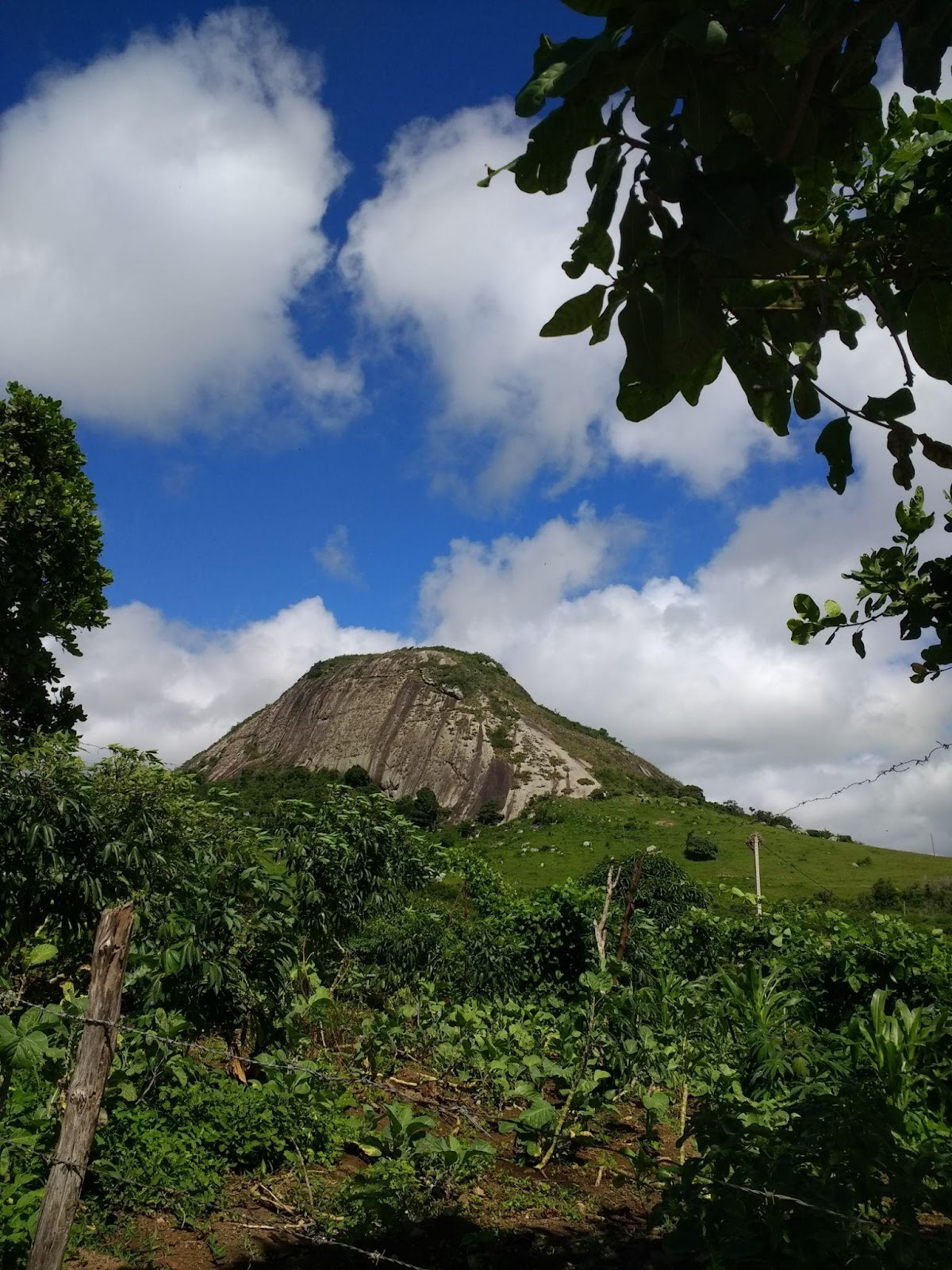 Paisagem com morro de pedra em Gravatá, PE. Céu azul com nuvens brancas.