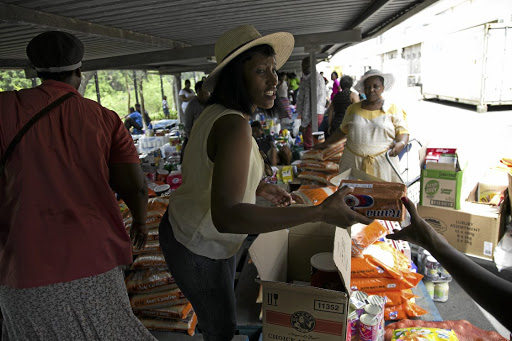 Princess Ngcobo passes around groceries as her fellow stokvel members receive their share in the parking lot at a store in Durban. / Rogan Ward