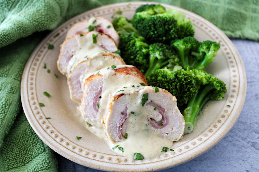 Sliced Chicken Cordon Bleu With Sauce on a plate with broccoli.