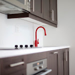 Dark brown cabinets with caesarstone countertop and a red kitchen faucet