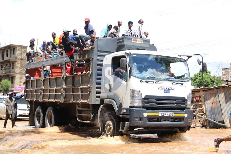 Kasarani residents hop on a lorry to cross a flooded road at a bridge connecting Mwiki and Kasarani on April 24, 2024.