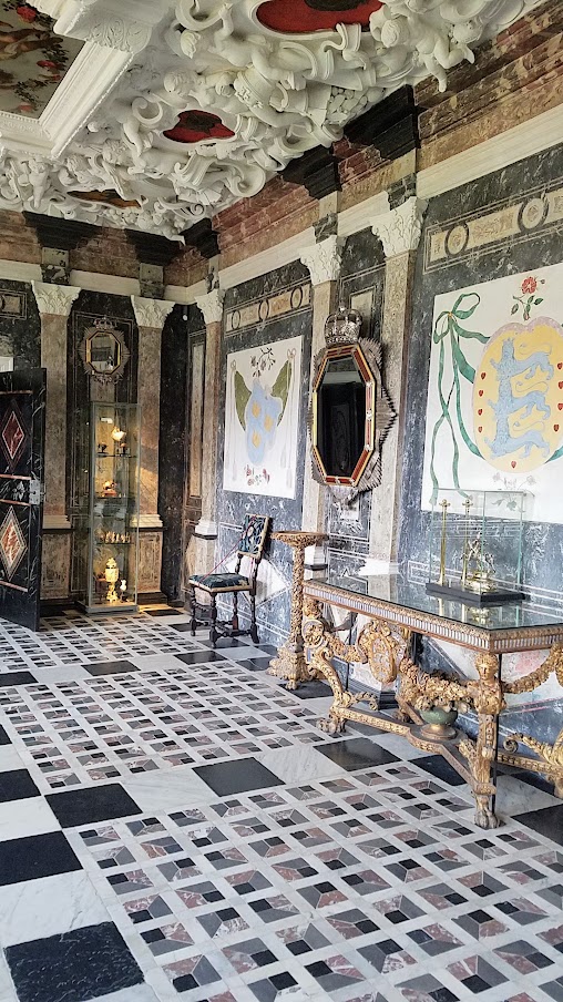 Visiting Rosenborg Castle in Copenhagen. This is the Marble Room - the ceiling paintings also show small, chubby, angelic child figures, carrying the Regalia and in the heart-shaped areas surrounding the paintings you can see parts of the Danish coat-of-arms and on the wall are the emblems of Norway, Denmark, and Sweden.