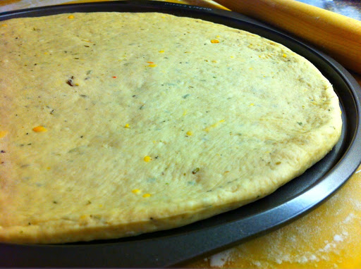 Pizza dough on a pizza pan with a rolling pin in the background.