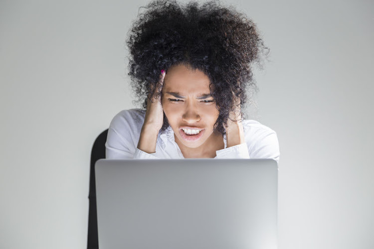 Close up of desperate office employee sitting at her workplace with laptop in room with gray walls. Concept of receiving bad news