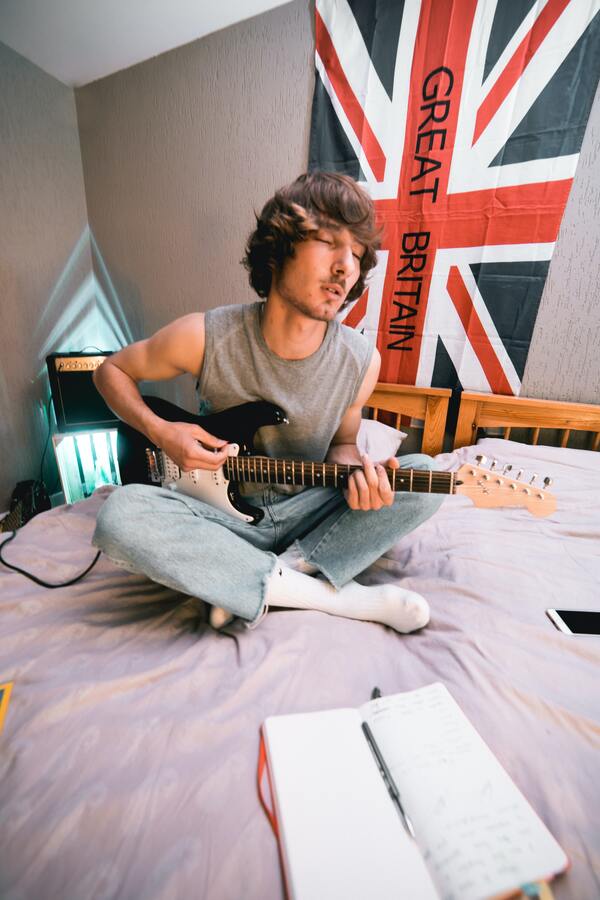 Um cara sentado na cama tocando guitarra