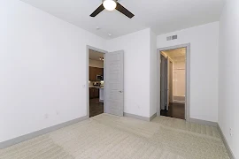 Light carpeting and walls in bedroom with ceiling fan with light fixture and attached bathroom