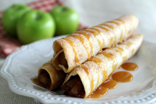 Caramel apple taquitos on a plate with caramel drizzled on top.